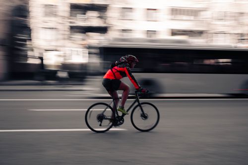 Free A cyclist rides swiftly down a bustling city street, capturing the essence of urban speed and motion. Stock Photo