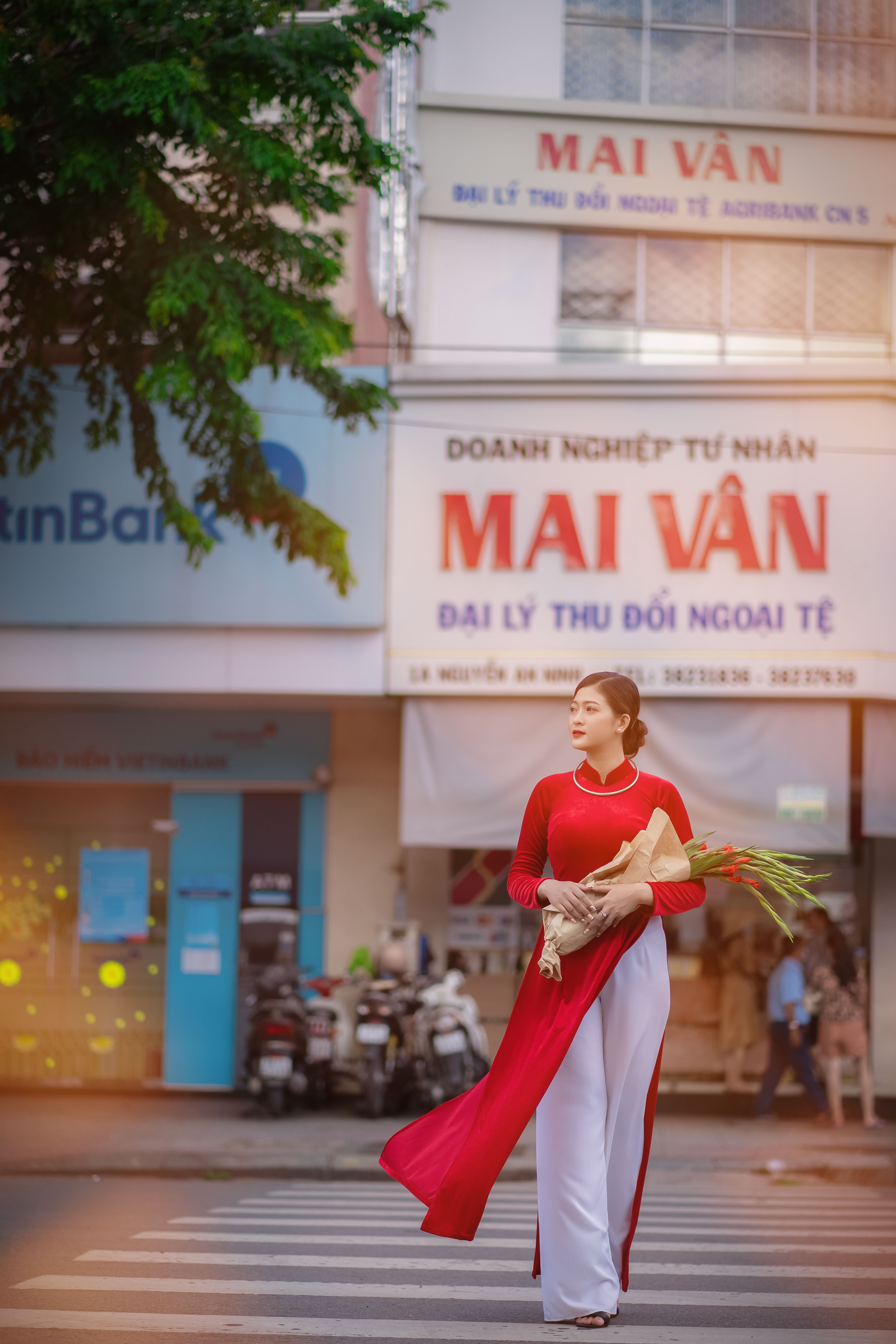 Woman in a vibrant red traditional dress crossing a bustling street lined with shops.