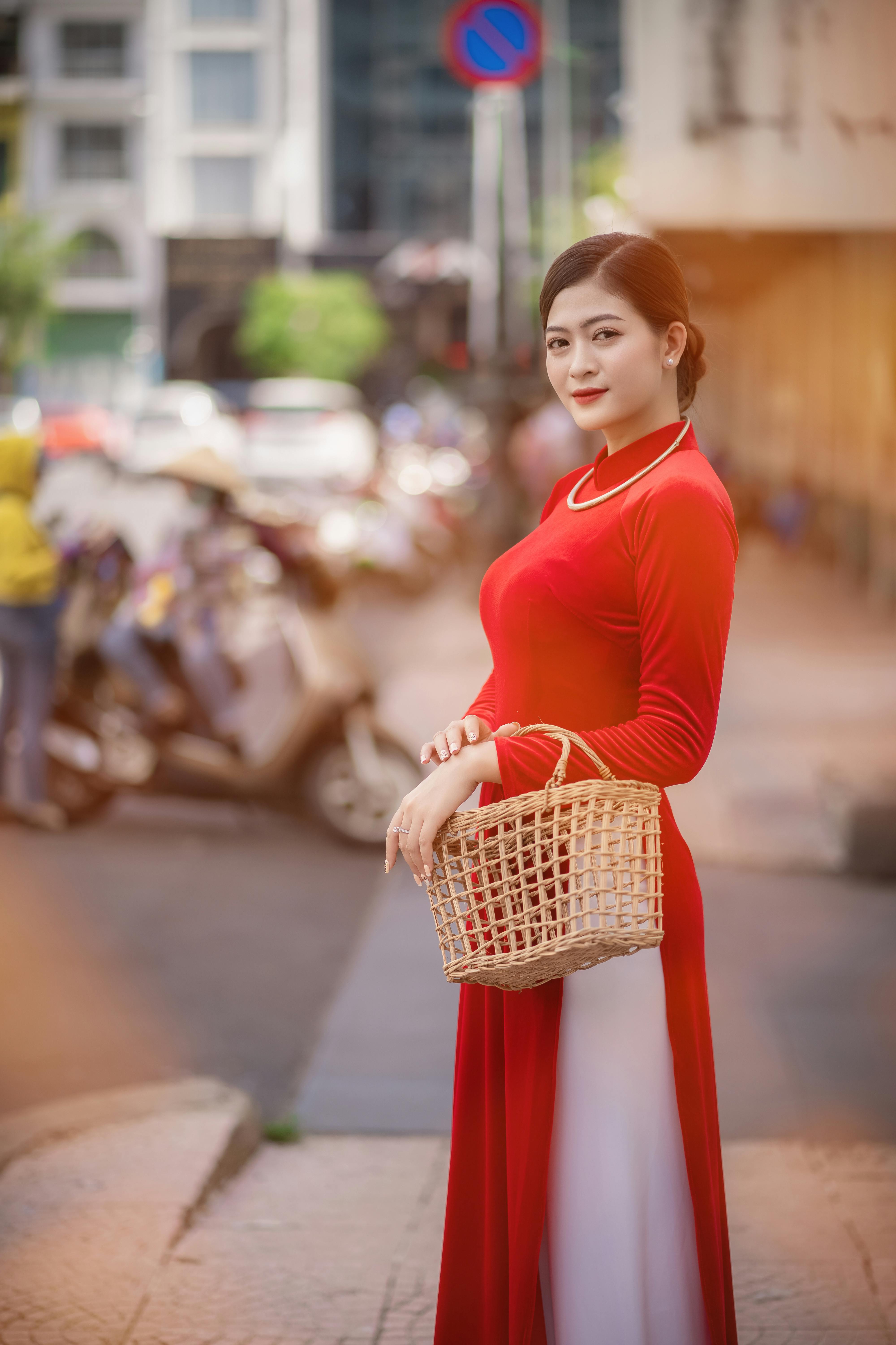A woman in a vibrant red ao dai poses gracefully on a bustling city street.