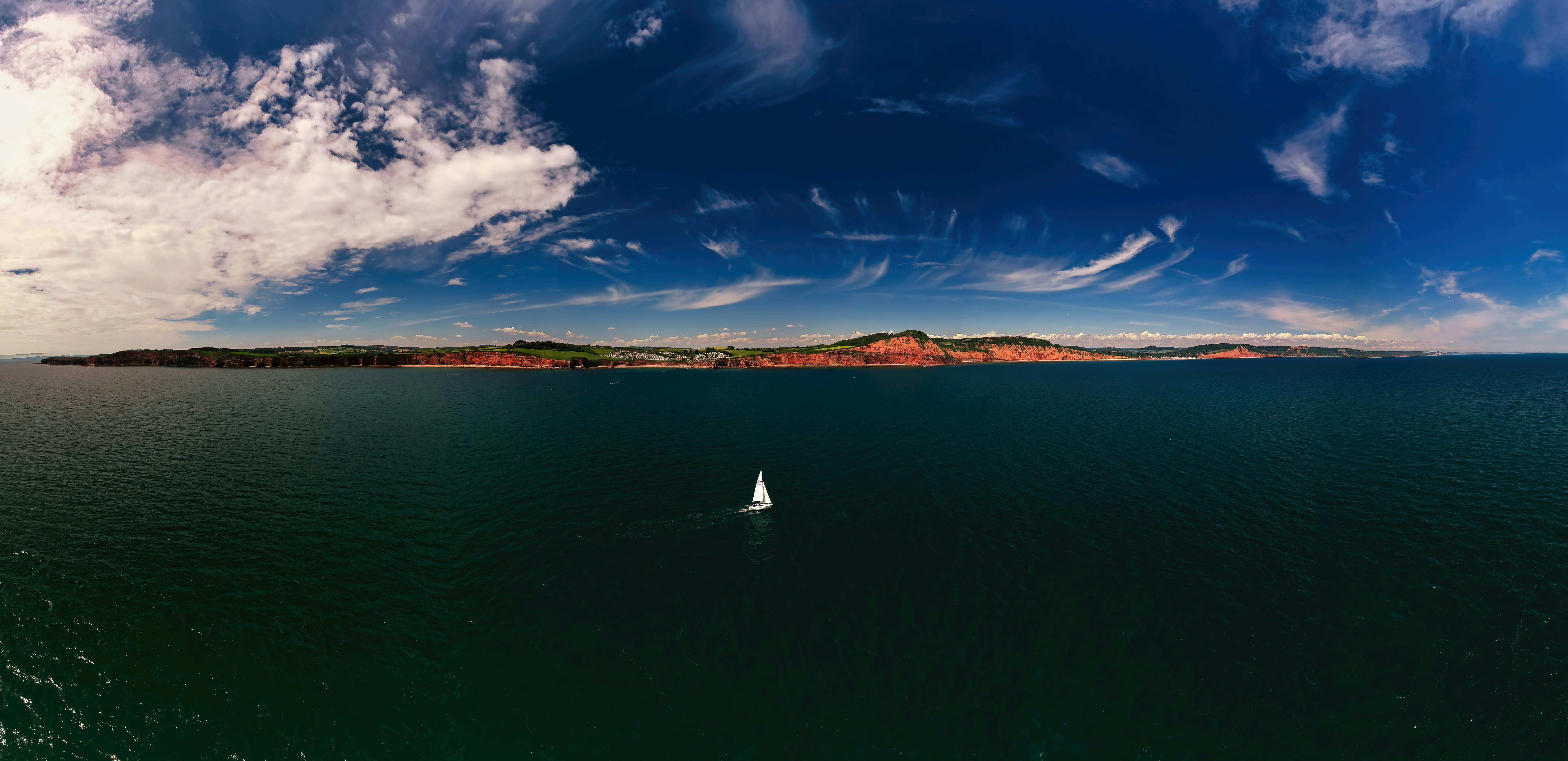 A serene aerial view of a sailboat in the vast ocean with dramatic skies.