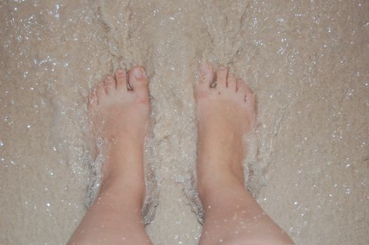 Close-up of bare feet standing on wet sandy beach shoreline, capturing ocean's gentle flow.