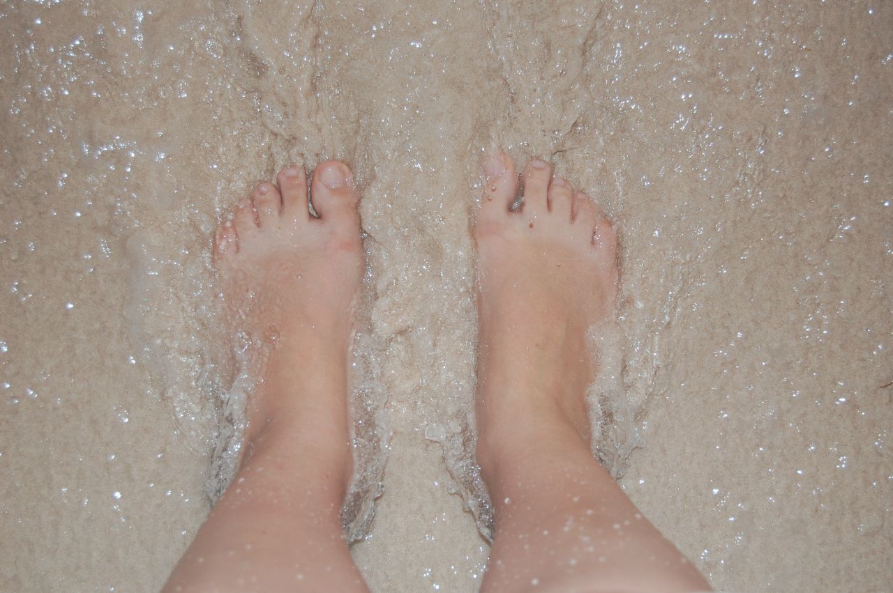 close up of bare feet standing on wet sandy beach shoreline capturing