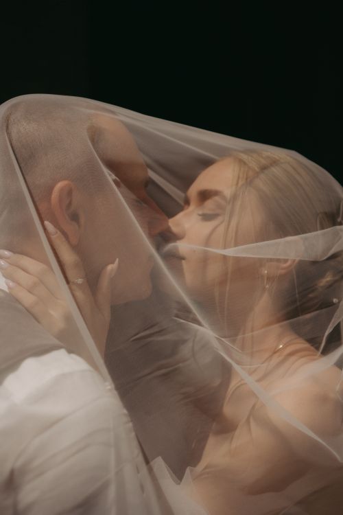 Free Close-up of a kissing couple wrapped in a wedding veil, capturing an intimate moment. Stock Photo