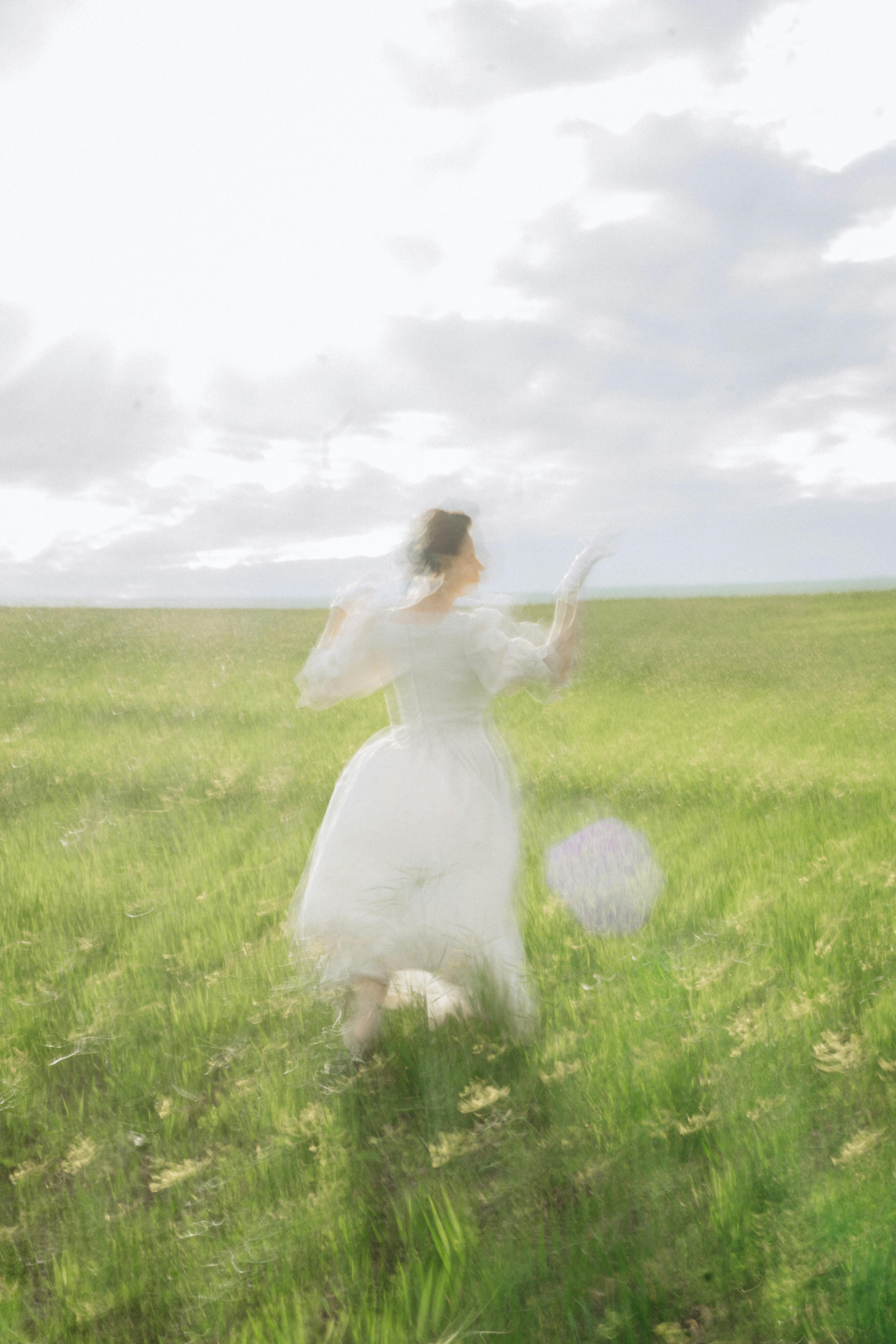 A woman in a flowing white dress runs through a grassy field, creating a dreamlike motion blur.