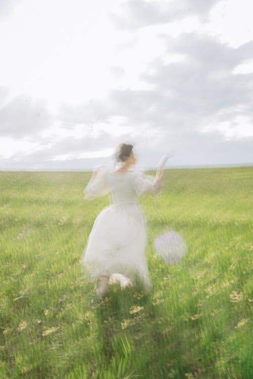 A Woman in White Dress Walking on Green Grass Field