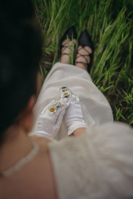 A woman wearing gloves holds small white flowers while sitting on grassy field.