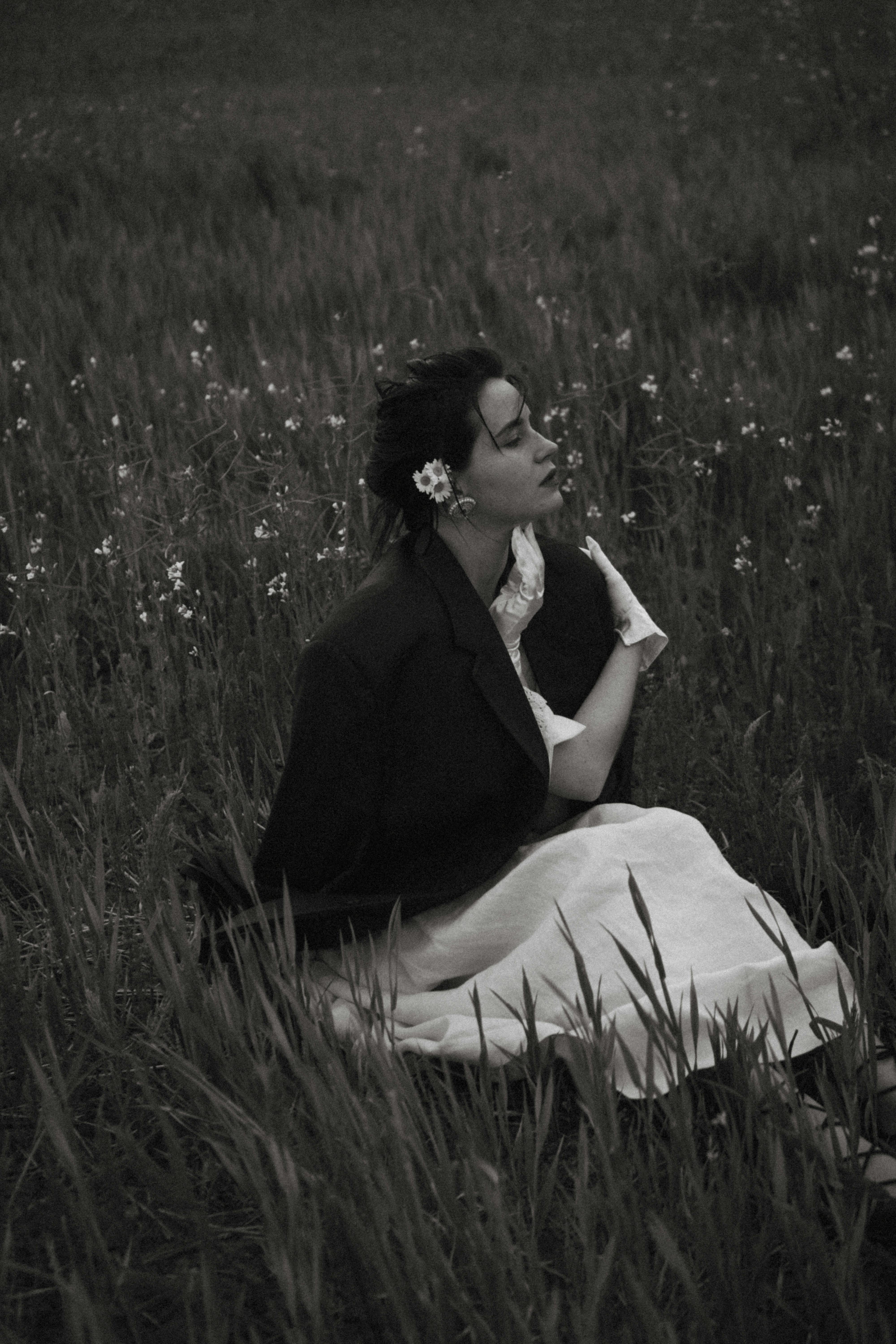 Elegant black and white photo of a woman sitting in a peaceful meadow.