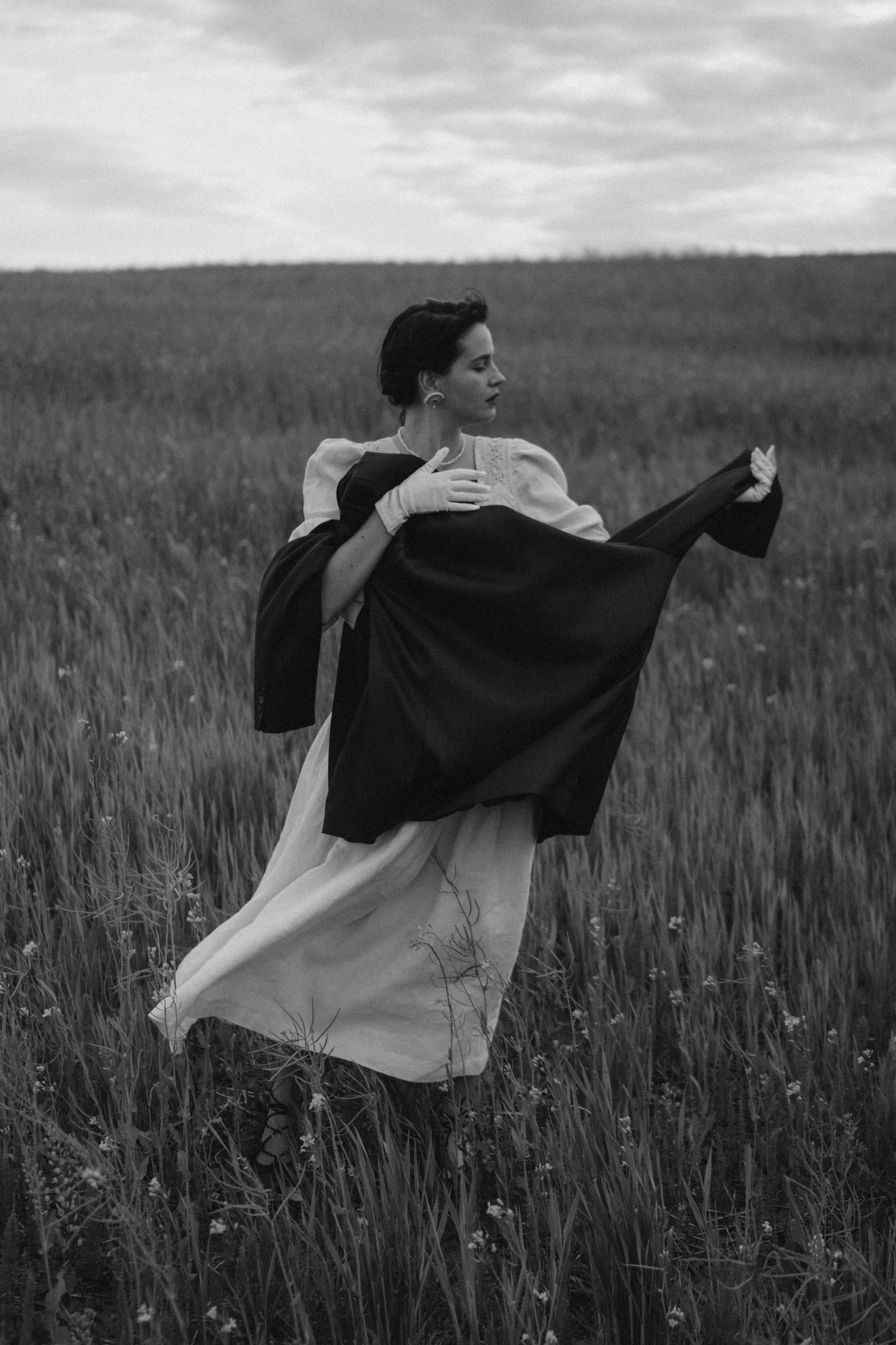 Artistic black and white photo of a woman in elegant fashion standing in a meadow.
