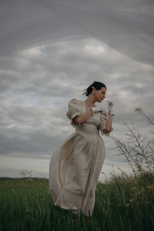 A Woman in White Dress Standing on Green Grass Field  