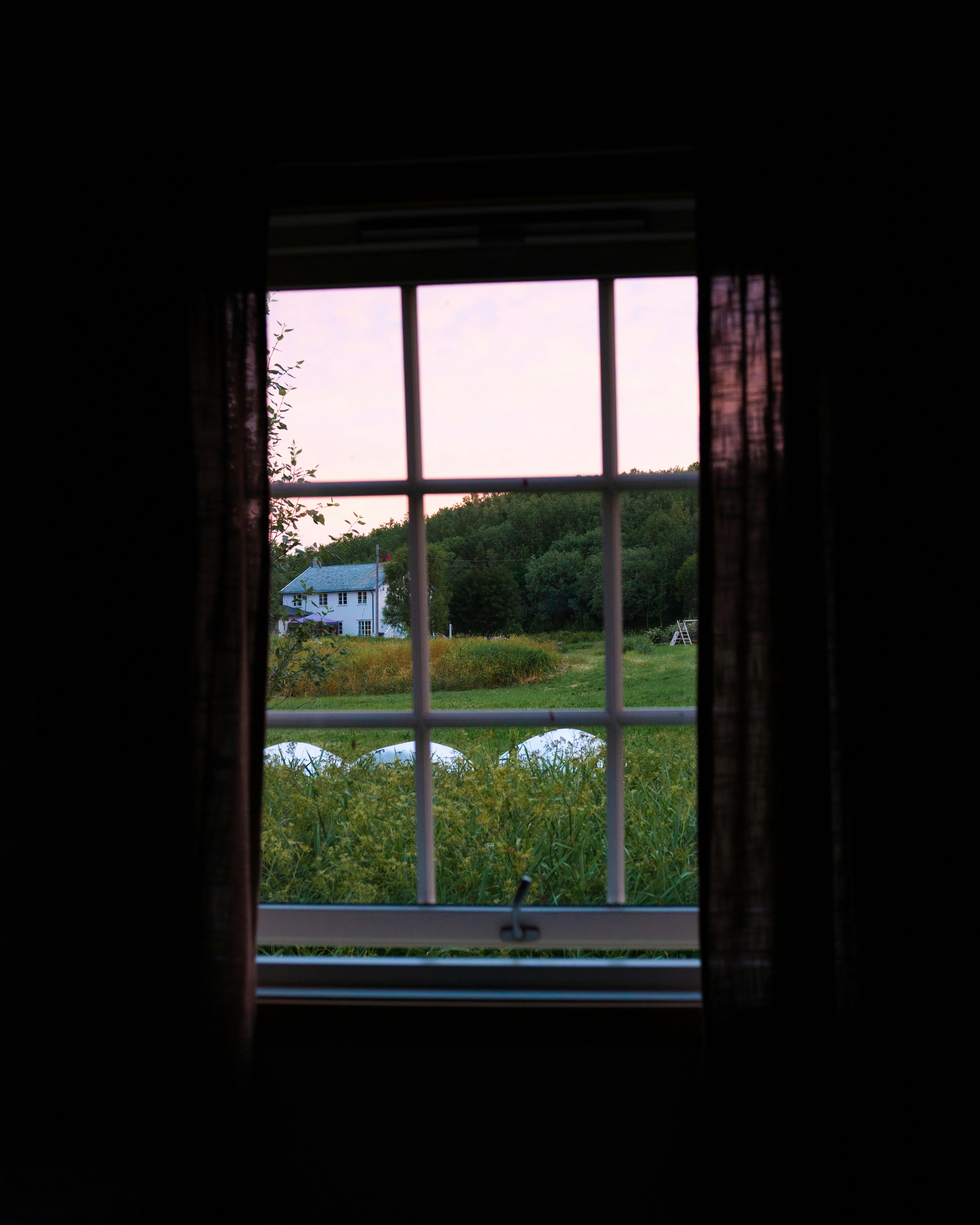 A tranquil countryside view from a cabin window in Nordland, Norway at sunset.