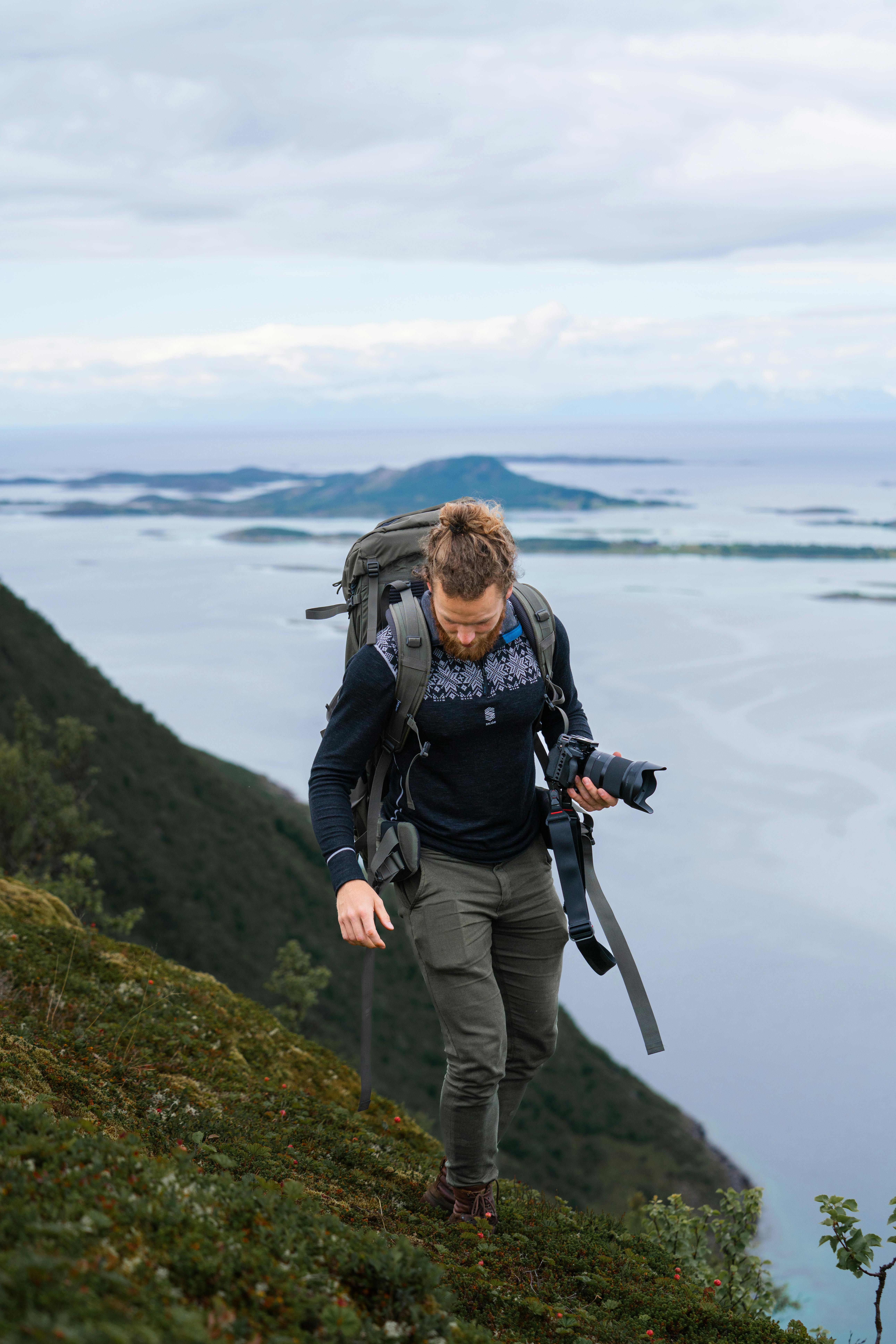 A photographer with a backpack hikes along the scenic coast of Nordland, Norway, capturing breathtaking views.