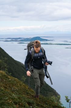 A photographer with a backpack hikes along the scenic coast of Nordland, Norway, capturing breathtaking views.