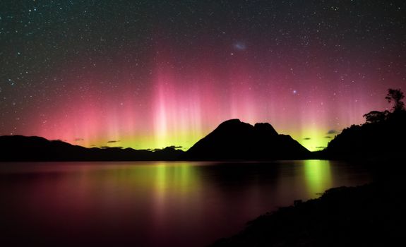 Stunning aurora display over Tasmania's lake with starry sky and mountain silhouette.