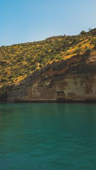 Calm bay with steep hillside covered in greenery under clear blue sky, showcasing natural serenity.