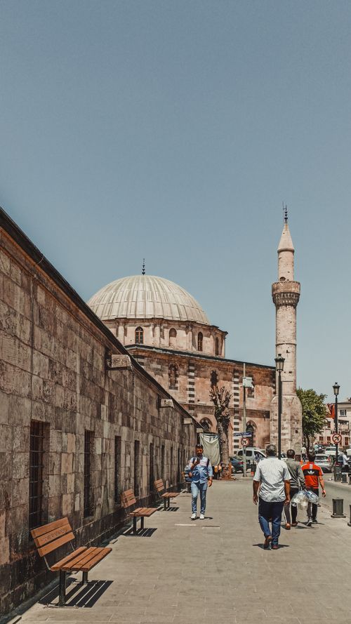 Free Outdoor scene of a bustling street beside a historical mosque, with people walking under a clear blue sky. Stock Photo