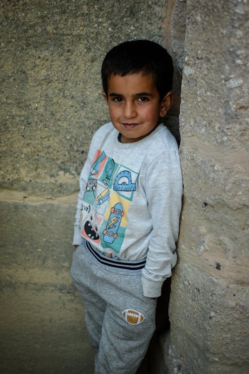 Free A Boy in Gray Sweater and Pants Leaning on the Concrete Wall Stock Photo