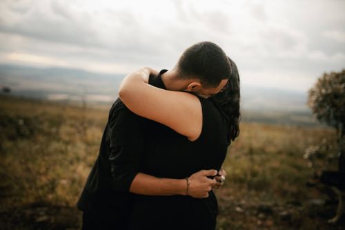 Free A couple embraces lovingly in a serene outdoor setting under a cloudy sky, evoking romance and tranquility. Stock Photo