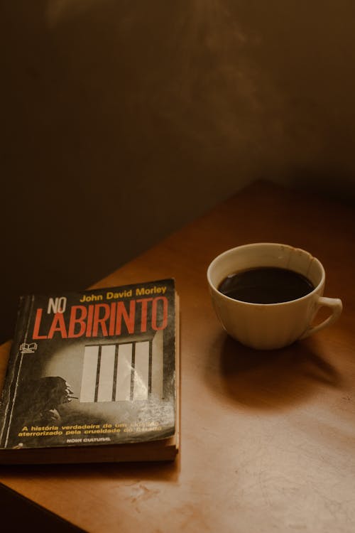 White Ceramic Mug with Coffee Beside an Old Book on Wooden Table