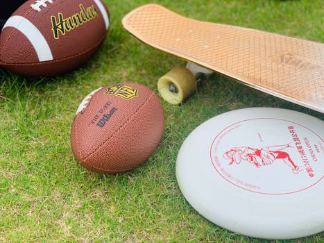 A close-up of sports equipment including a football, skateboard, and frisbee on grass.