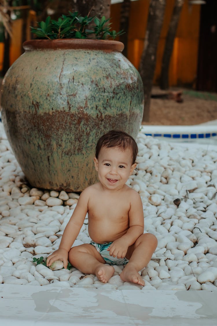 Baby Boy Sitting In A Diaper On Stones And Smiling 