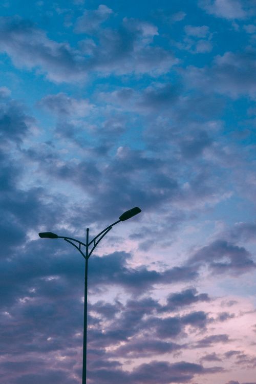 Free A street lamp silhouetted against a vibrant twilight sky filled with clouds. Stock Photo