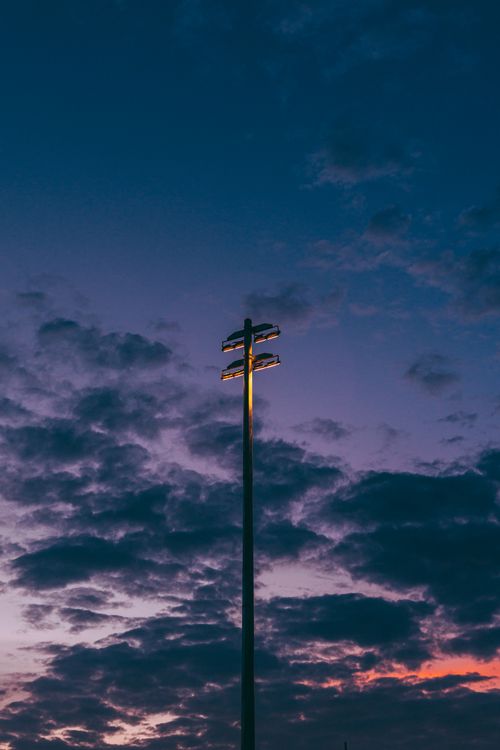 Free A stadium light post stands against a dramatic twilight sky with clouds, creating a moody atmosphere. Stock Photo