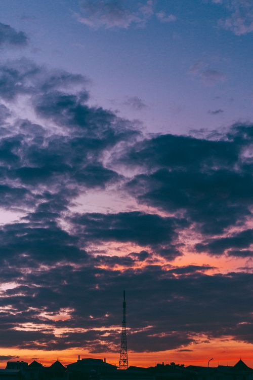 Free Vibrant sunset with dramatic clouds and a silhouetted tower. Perfect for backgrounds or weather-themed content. Stock Photo