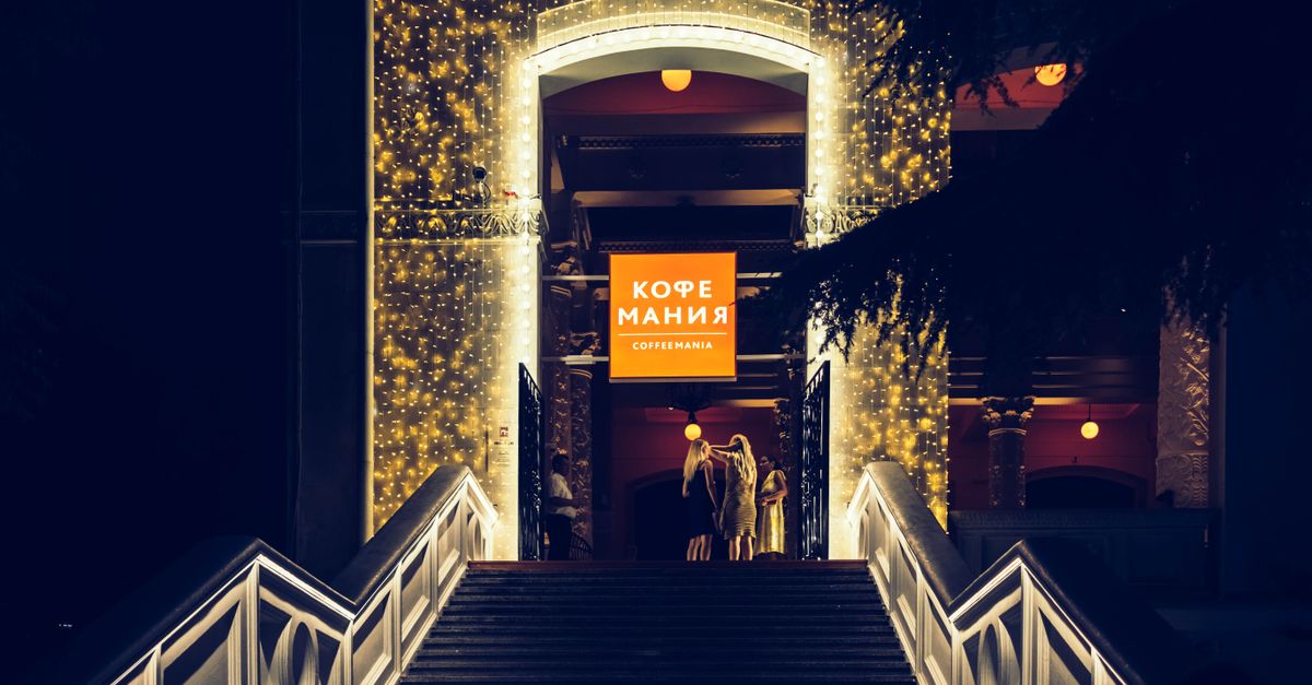 A beautifully illuminated cafe entrance in Sochi, Russia, captured at night with festive lights and people.