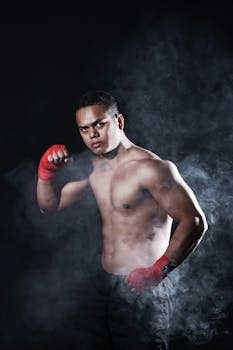 Shirtless male boxer posing in a studio with dramatic smoke effect, highlighting muscular build and focus.