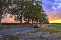 一辆汽车沿着绿树成荫的乡村道路行驶，沐浴在充满活力的日落中