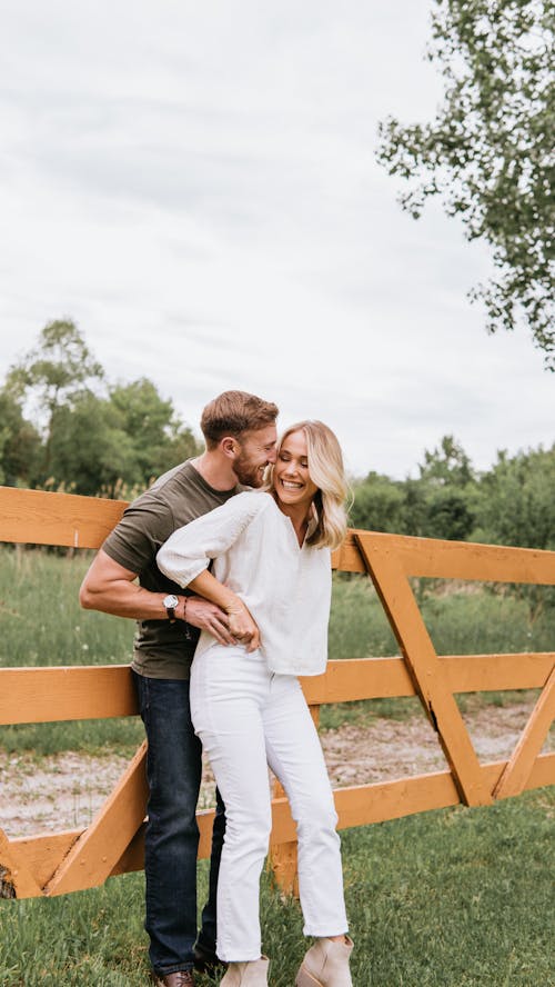 Free Smiling Couple Hugging Outdoors Leaning on a Wooden Fence  Stock Photo