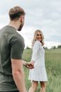 Man and Woman Holding Hands While Walking on Green Grass Field