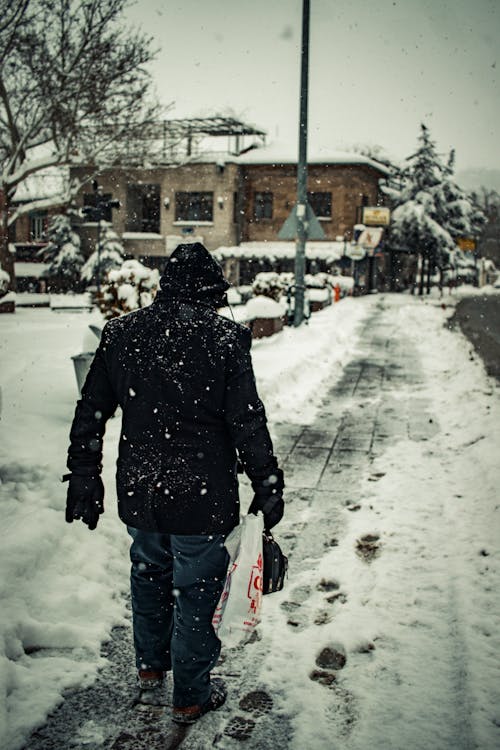 A Back View of a Person Walking on the Street while Snowing