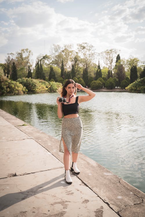 Stylish Woman in Black Tank Top and Floral Skirt standing by the Lakeside 