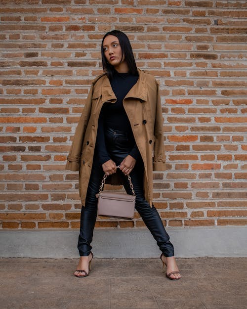 Stylish Woman in Brown Coat standing against a Brick Wall 