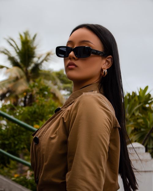 Free Confident woman in sunglasses standing outdoors with lush greenery backdrop. Stock Photo