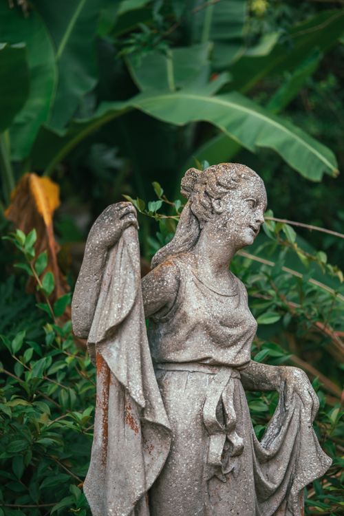 Free Close-up of an intricately carved stone statue surrounded by lush greenery in a garden. Stock Photo