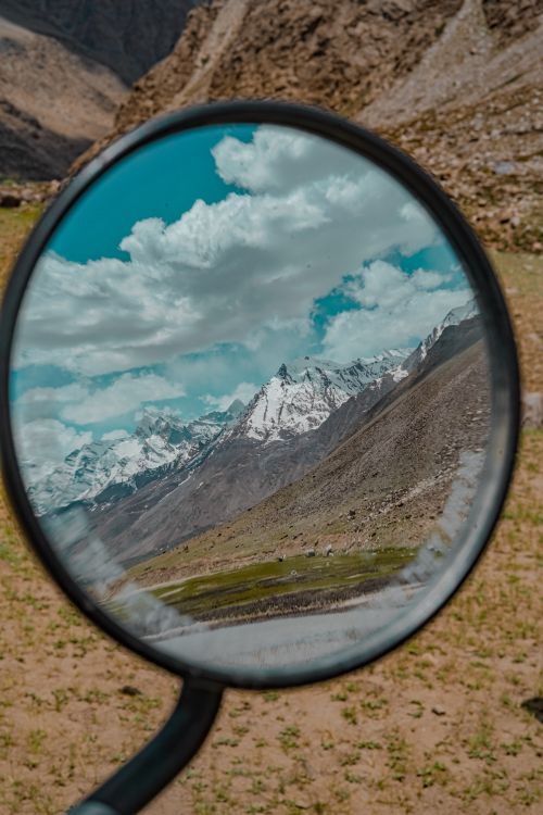 Free A stunning mountain range reflected in a motorcycle side mirror under a clear sky. Stock Photo