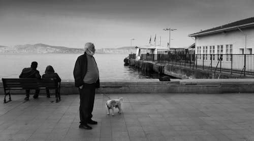 Grayscale Photo of a Man Waiting with His Dog