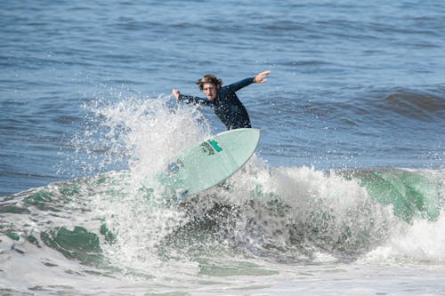 A Man in Black Wetsuit Surfing on the Beach