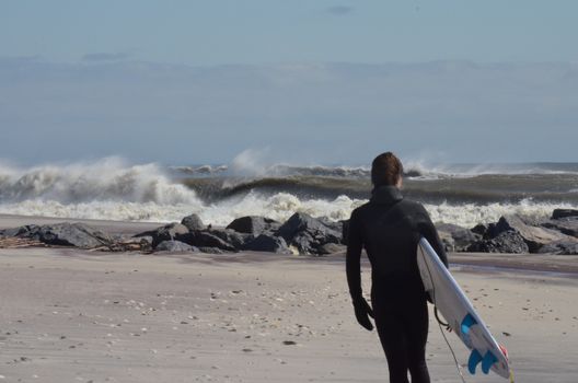 Surfer in wetsuit heads towards ocean waves, ready for an adventure.