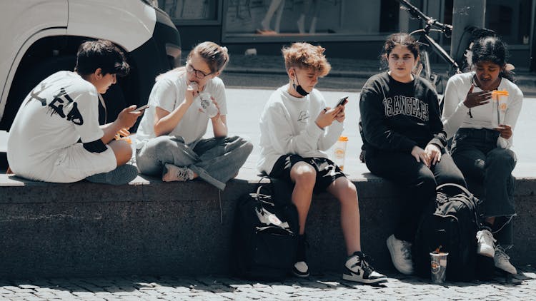 A Group Of Teenagers Sitting On The Street While Having Conversation