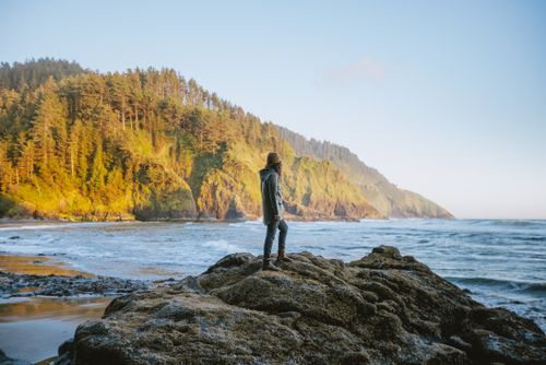 Free Person enjoying a serene coastal view with lush forested hills in Oregon. Stock Photo