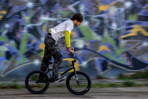 Free A person riding a BMX bike past a colorful graffiti wall, capturing motion and urban energy. Stock Photo