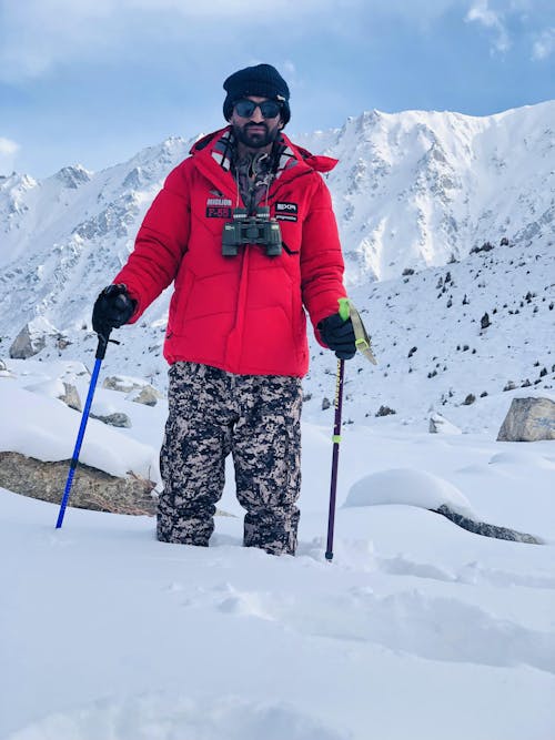 A Man in Red Jacket Standing on a Snow Covered Ground while Holding a Trekking Poles
