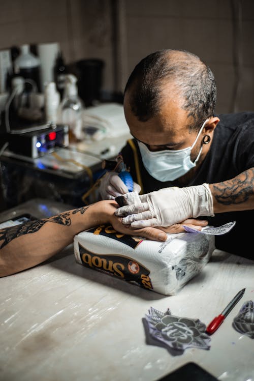 A Man Wearing Face Mask while Doing Tattoo