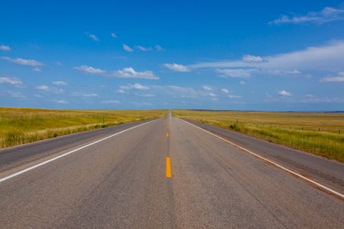 A Concrete Road Between Green Grass Field Under the Blue Sky and White Clouds