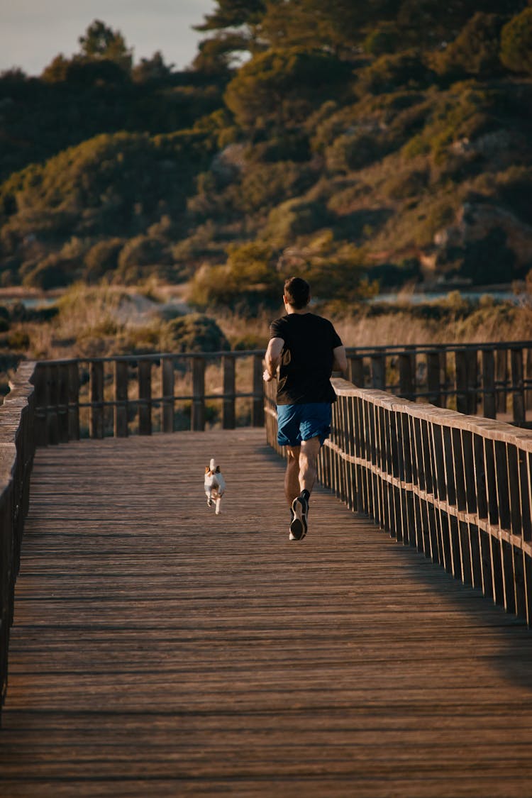 A Man In Black Shirt Jogging With His Dog