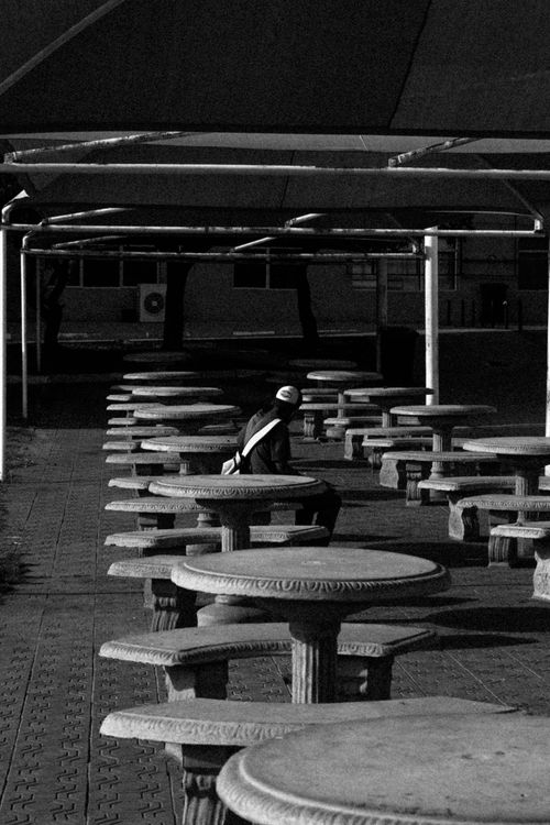 Free Black and white photo of an outdoor seating area with a solitary figure sitting alone. Stock Photo
