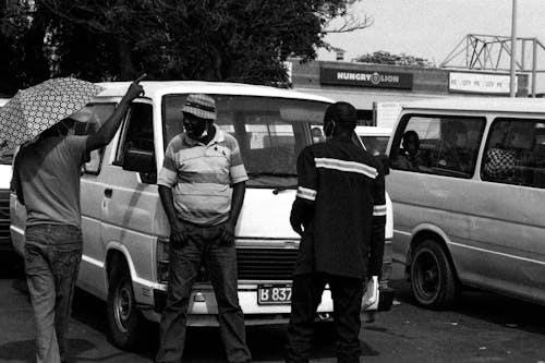 Grayscale Photo of People Talking Near a Van